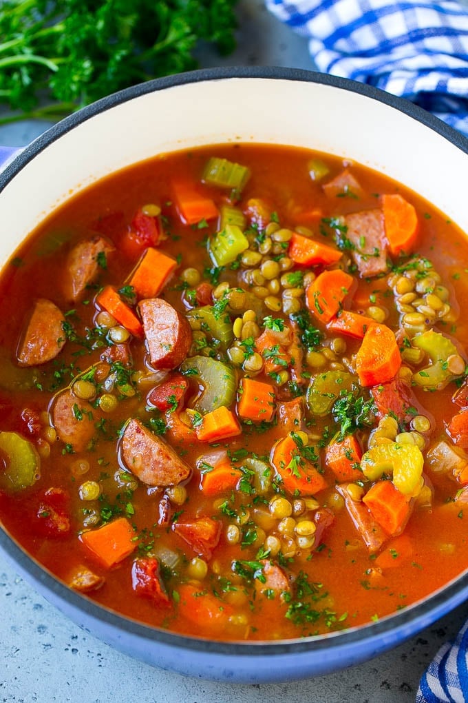A pot of lentil soup flavored with vegetables, tomatoes and smoked sausage, then garnished with chopped parsley.