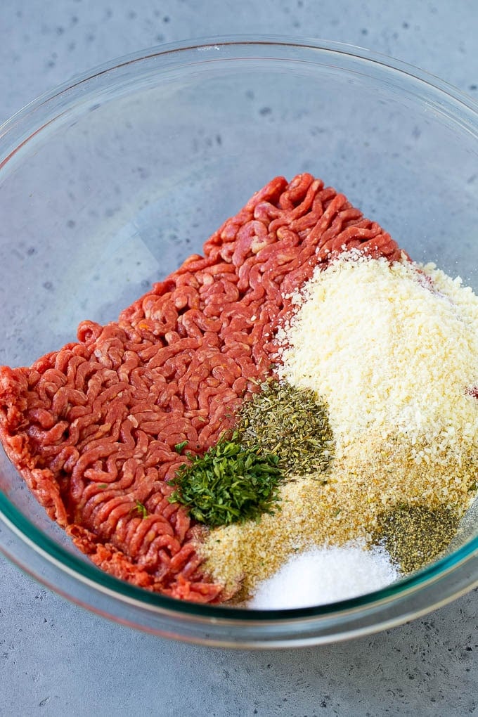 Ground beef, breadcrumbs, parsley, herbs and parmesan cheese in a mixing bowl.