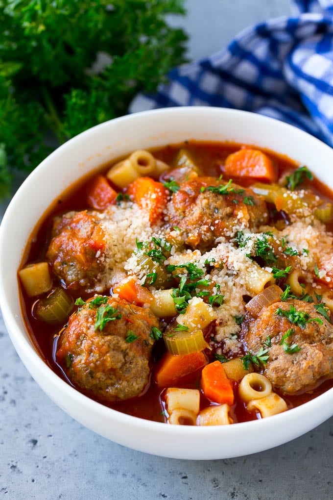 A bowl of meatball soup topped with chopped parsley and grated cheese.