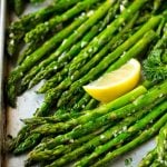 Roasted asparagus on a sheet pan, topped with chopped parsley and garnished with lemon wedges.