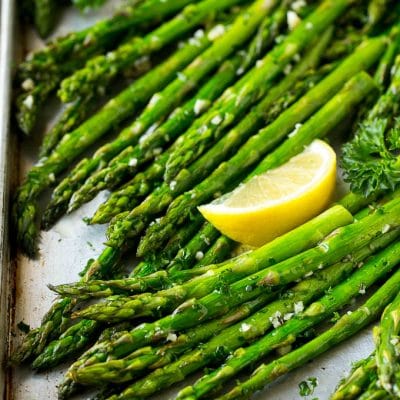 Roasted asparagus on a sheet pan, topped with chopped parsley and garnished with lemon wedges.