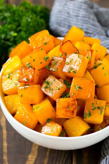 A bowl of roasted butternut squash made with brown sugar and maple syrup, then garnished with chopped parsley.