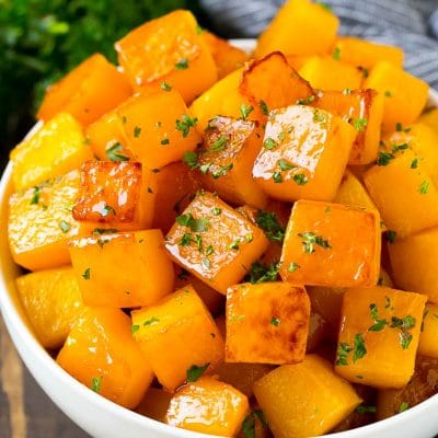 A bowl of roasted butternut squash made with brown sugar and maple syrup, then garnished with chopped parsley.