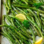 Roasted green beans on a sheet pan garnished with lemon and parsley.