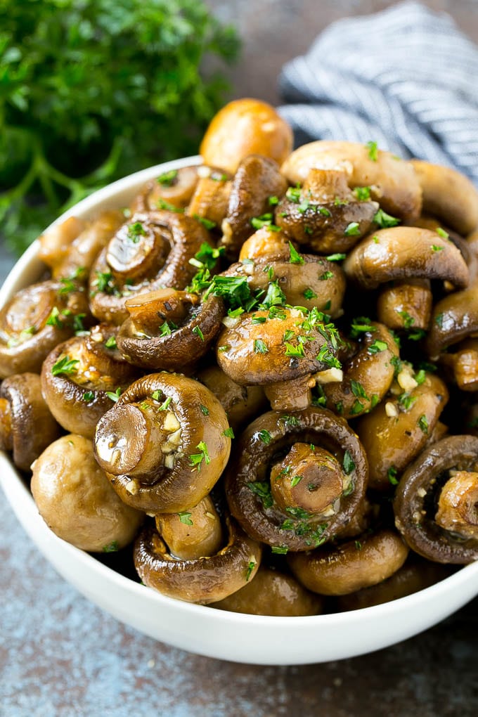 A bowl of roasted mushrooms coated in a garlic and herb butter and topped with fresh parsley.