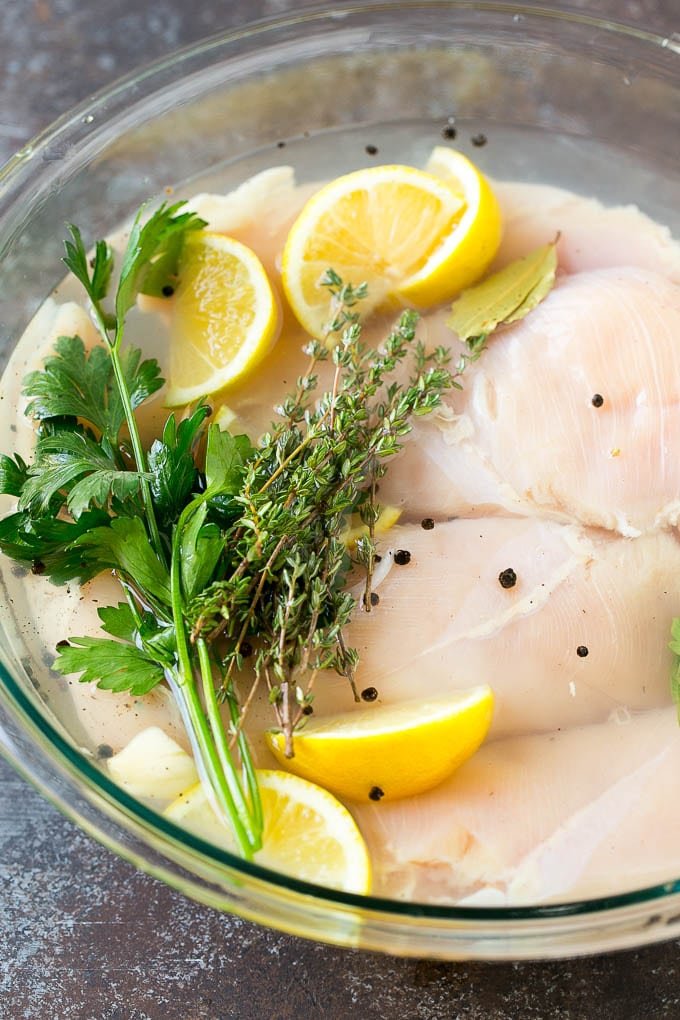 Chicken breasts in a bowl of brine with lemon and herbs.
