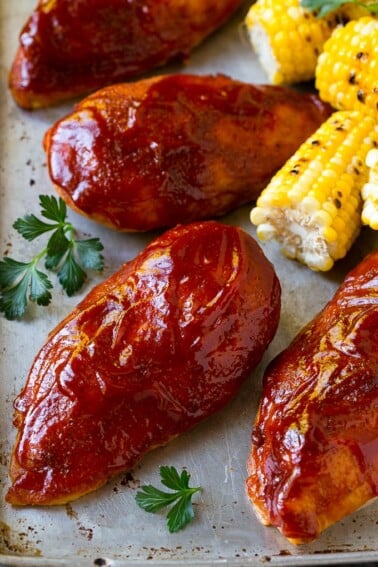 Smoked chicken breasts on a sheet pan with corn on the corn and fresh herbs.