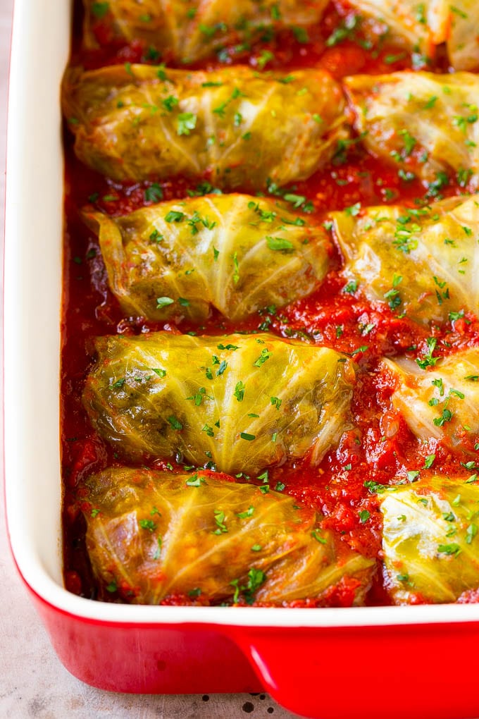 Stuffed cabbage rolls in a baking dish in a pool of tomato sauce.
