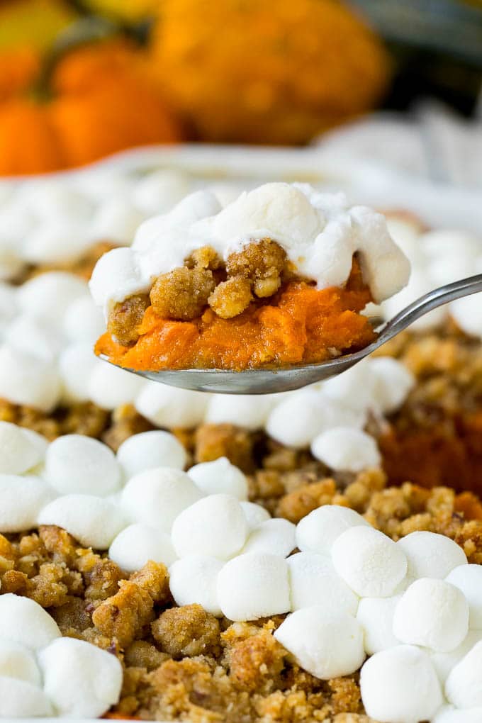 A serving spoon holding up a portion of sweet potato casserole with marshmallows.