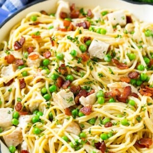 A skillet of turkey pasta carbonara with peas and bacon in a creamy sauce.