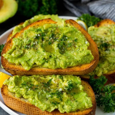 A plate of avocado toast with fresh parsley as a garnish.