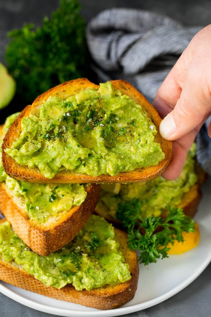 A hand holding a piece of homemade avocado toast.