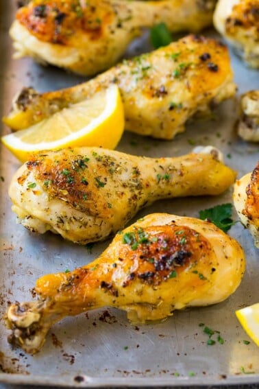 Baked chicken drumsticks flavored with garlic and herbs, then garnished with lemon wedges and parsley.