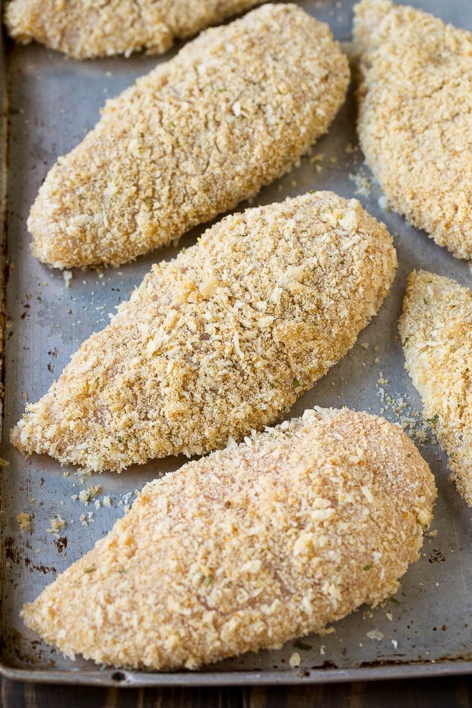 Chicken breasts coated in parmesan breading on a sheet pan.