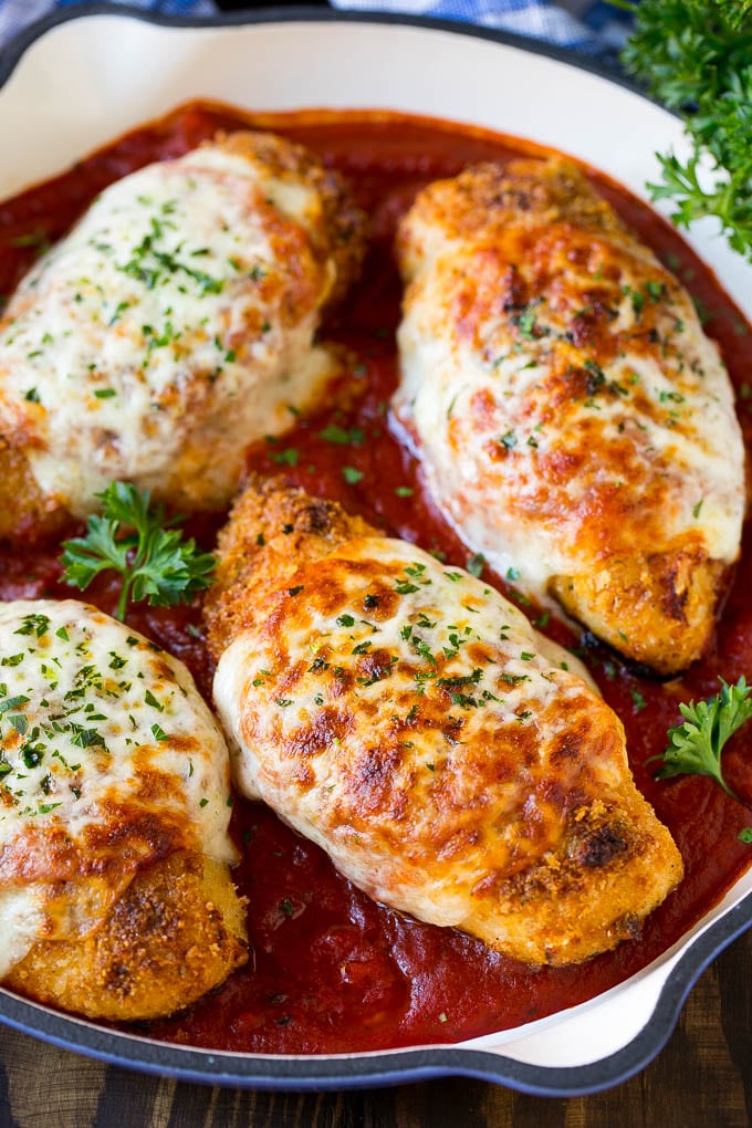 A skillet of baked chicken parmesan with crispy chicken breasts, marinara sauce and melted cheese.