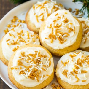 Eggnog cookies topped with frosting and gold sprinkles on a serving plate.