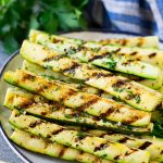 Grilled zucchini on a serving plate topped with fresh parsley.