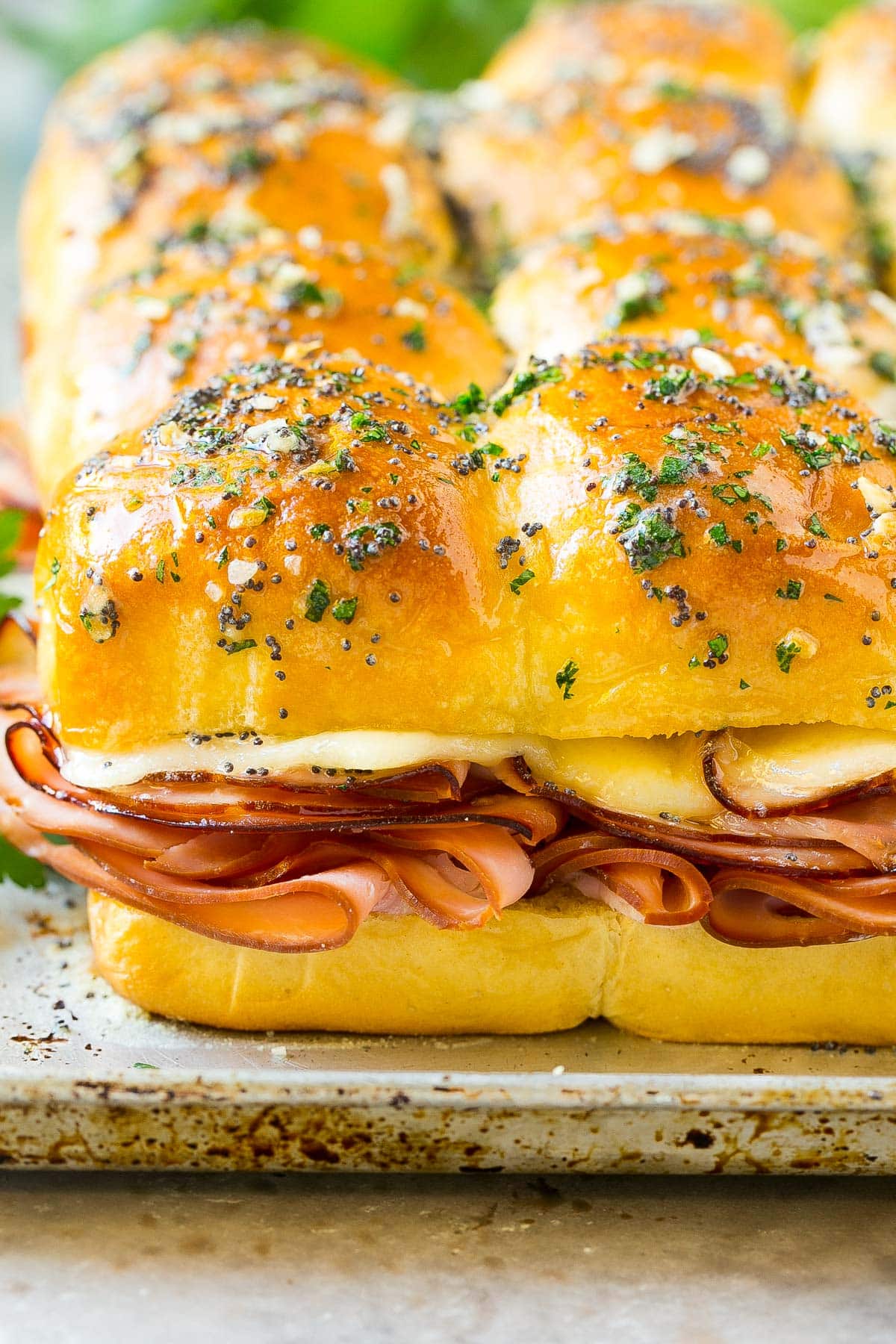 Baked ham and cheese sliders on a pan, topped with parsley.