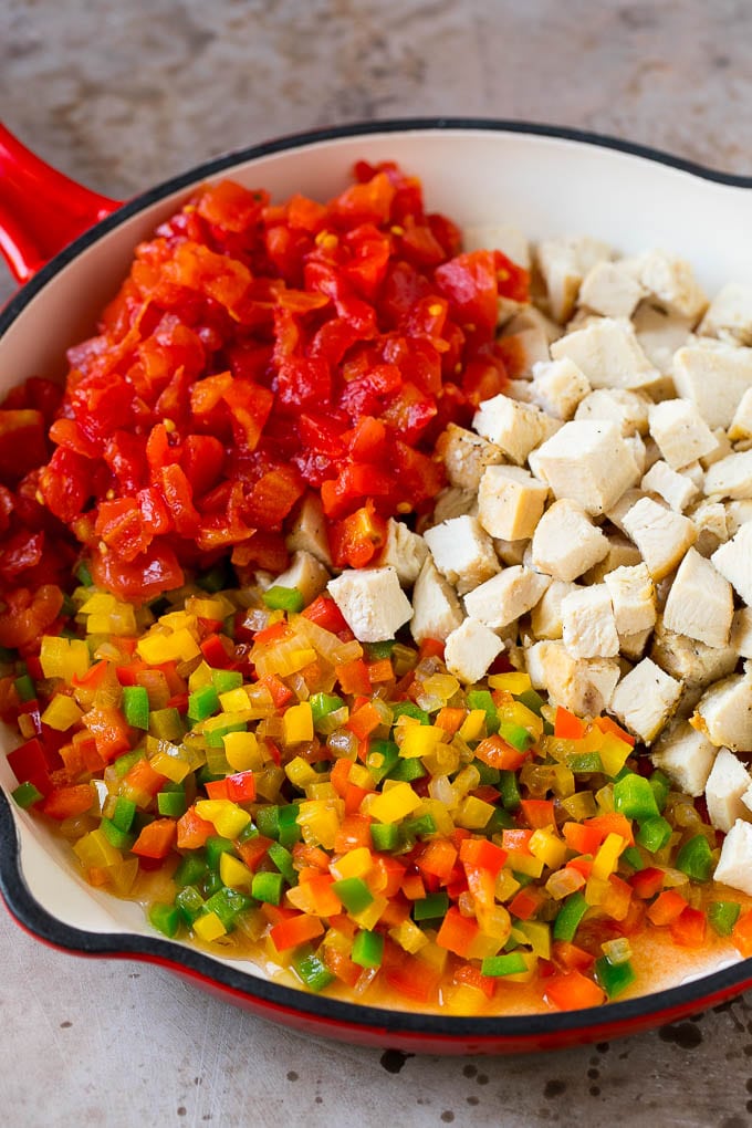 Cubed chicken, cooked peppers and tomatoes in a skillet.