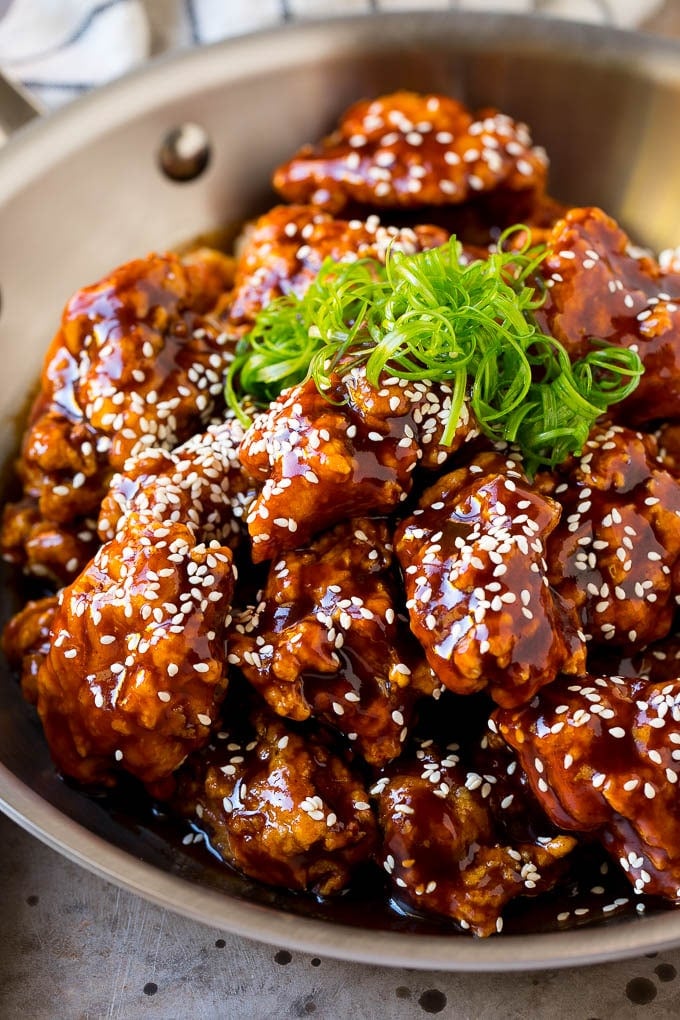 A pan of Korean fried chicken coated in a sweet and spicy sauce then garnished with sesame seeds.