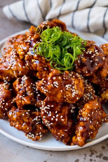 Korean fried chicken on a serving plate topped with curly green onions.