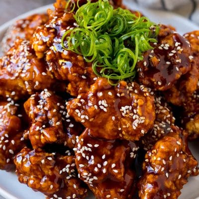 Korean fried chicken on a serving plate topped with curly green onions.