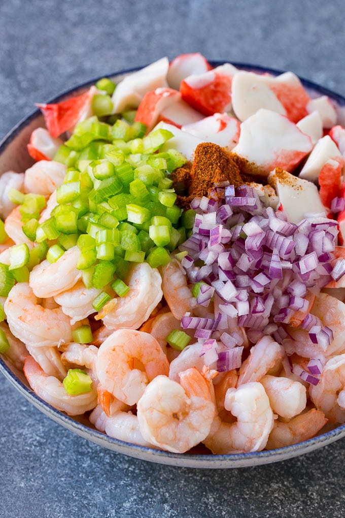 Shrimp, imitation crab, red onion, celery and Old Bay seasoning in a bowl.