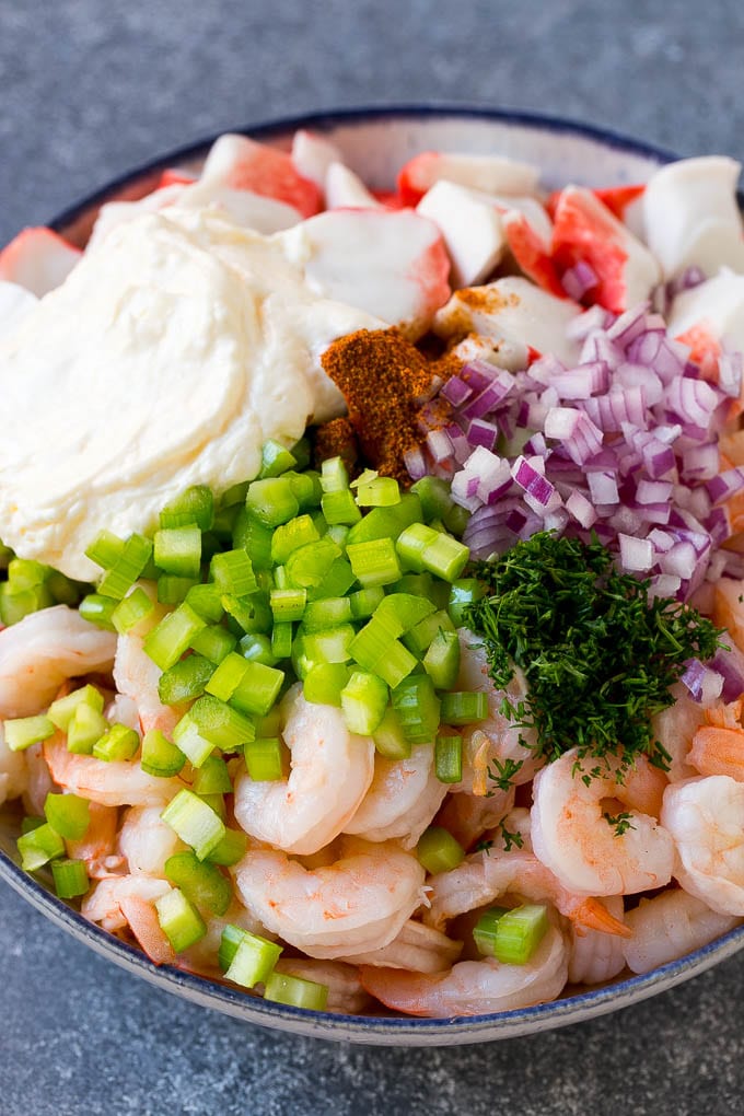 A bowl of shrimp, imitation crab, vegetables, dill and mayonnaise.