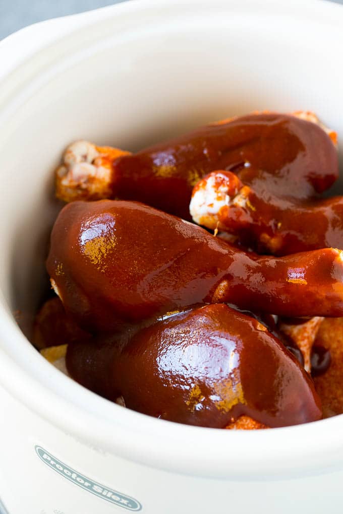 A crock pot of chicken drumsticks coated in BBQ sauce.