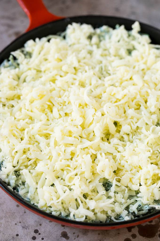 A skillet of unbaked spinach dip topped with shredded cheese.