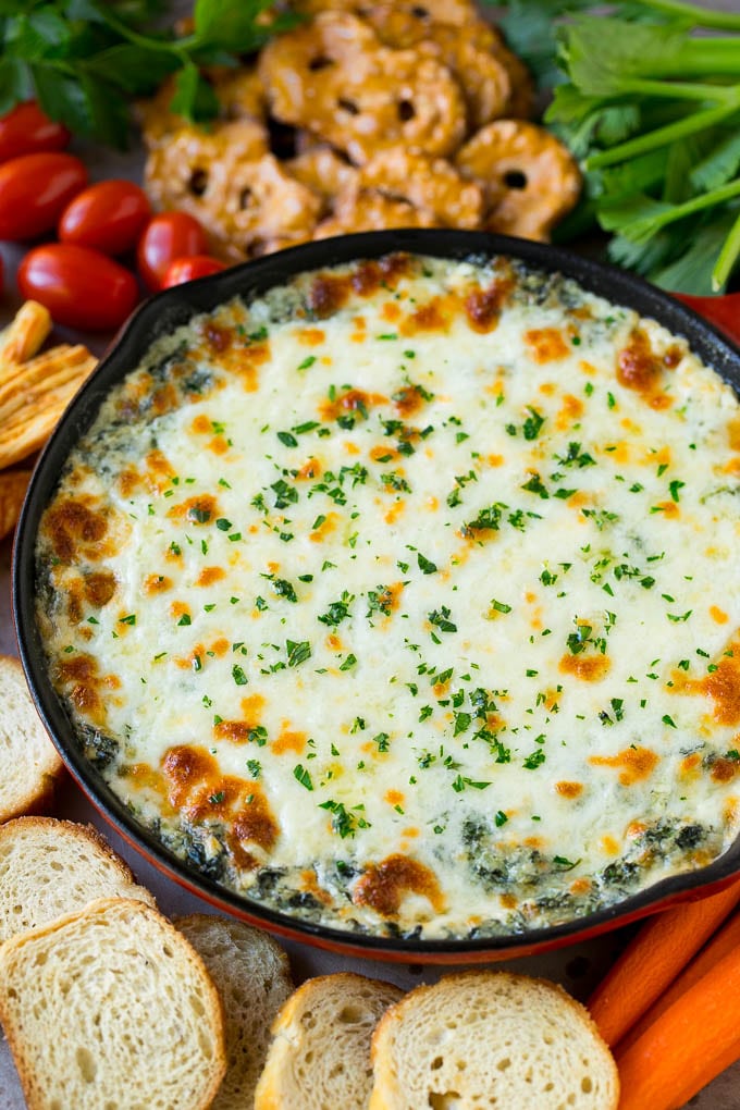 A skillet of hot spinach dip garnished with parsley and served with crackers, bread and vegetables.