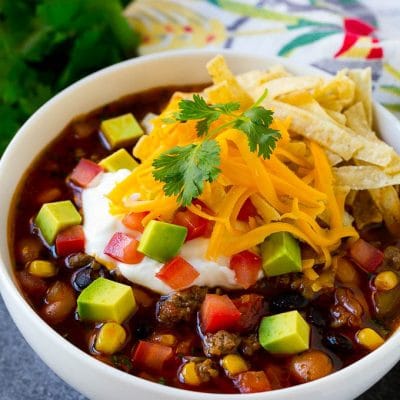 A bowl of taco soup topped with tortilla strips, sour cream, cheese and avocado.