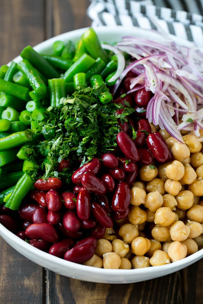 Three types of beans and red onion topped with salad dressing and chopped parsley.