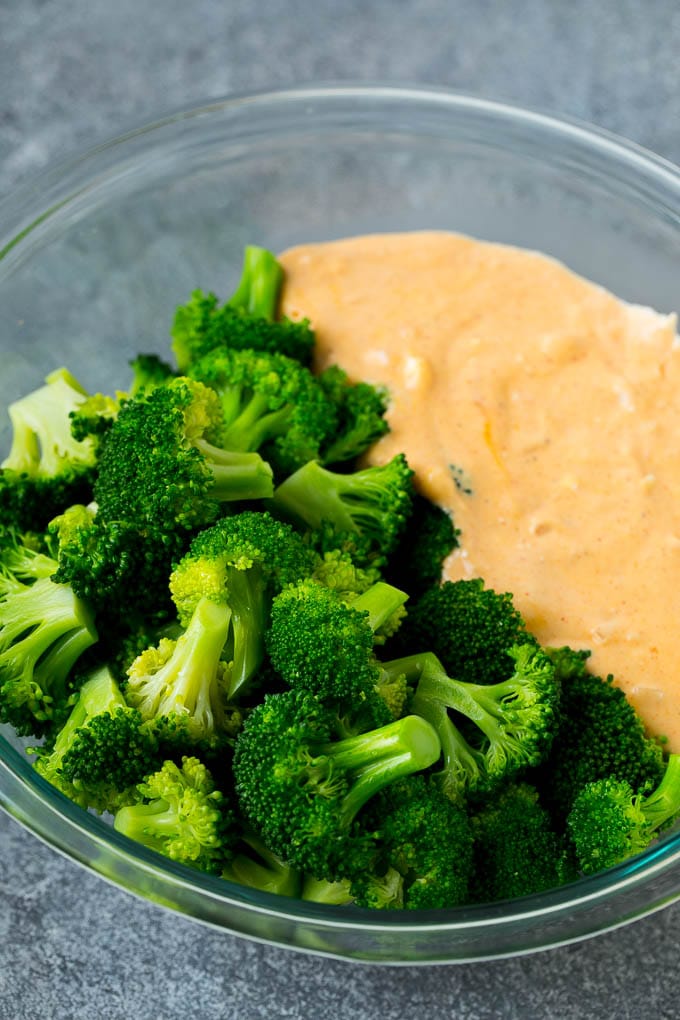 Cooked broccoli florets and cheese sauce in a mixing bowl.
