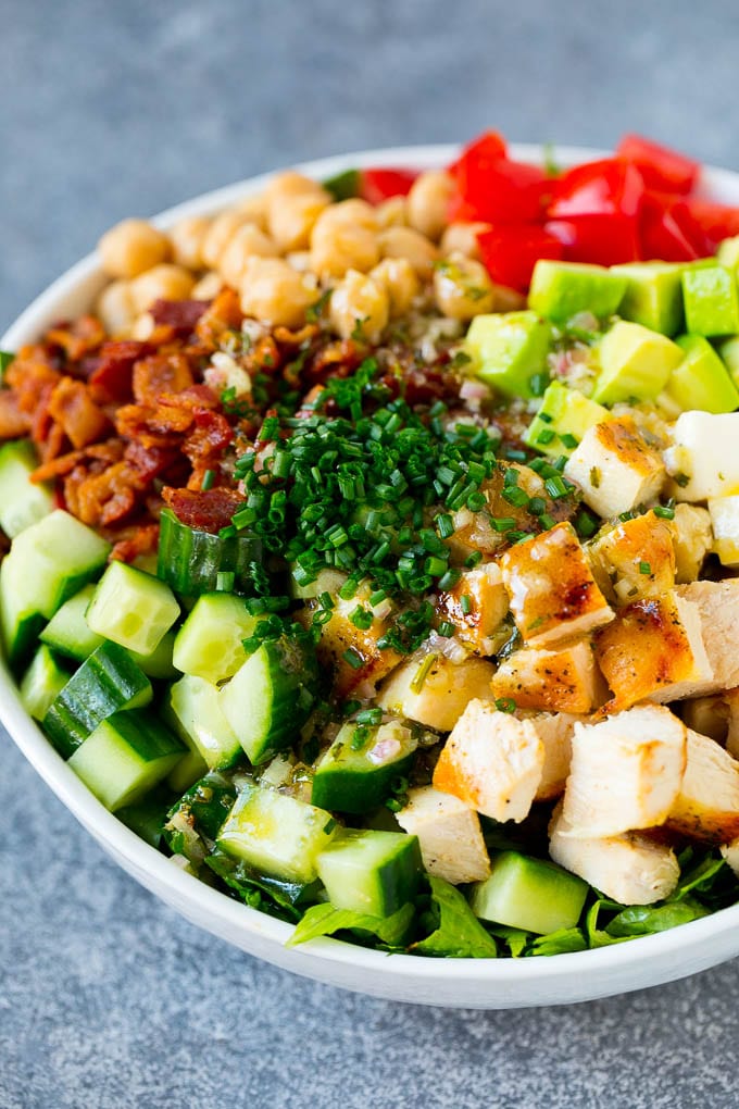 Ingredients for chopped chicken salad in a serving bowl, drizzled with homemade dressing and sprinkled with chives.