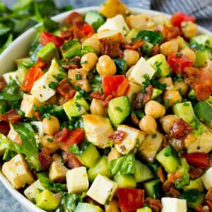 A bowl of chopped salad made with chicken, lettuce, tomato, cucumber, bacon and chickpeas.