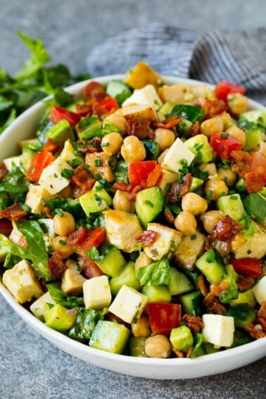 A bowl of chopped salad made with chicken, lettuce, tomato, cucumber, bacon and chickpeas.