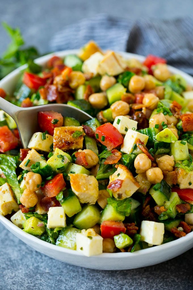 A serving spoon in a bowl of chopped salad garnished with fresh chives.