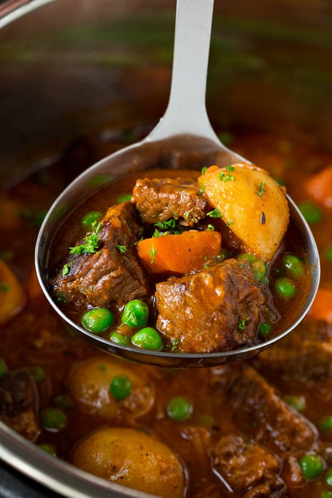 A ladle full of Instant Pot beef stew with chunks of beef, carrots, potatoes and peas.