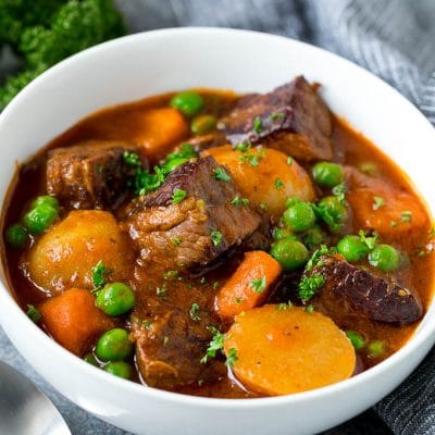 A bowl of Instant Pot beef stew with cubes of meat, potatoes, carrots, onions and peas.