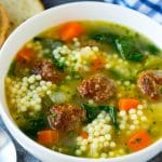 A bowl of Italian wedding soup with meatballs, carrots, spinach and pasta.