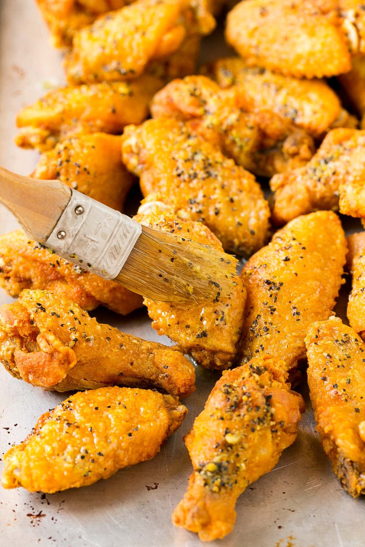 A brush putting seasoned butter onto chicken wings.