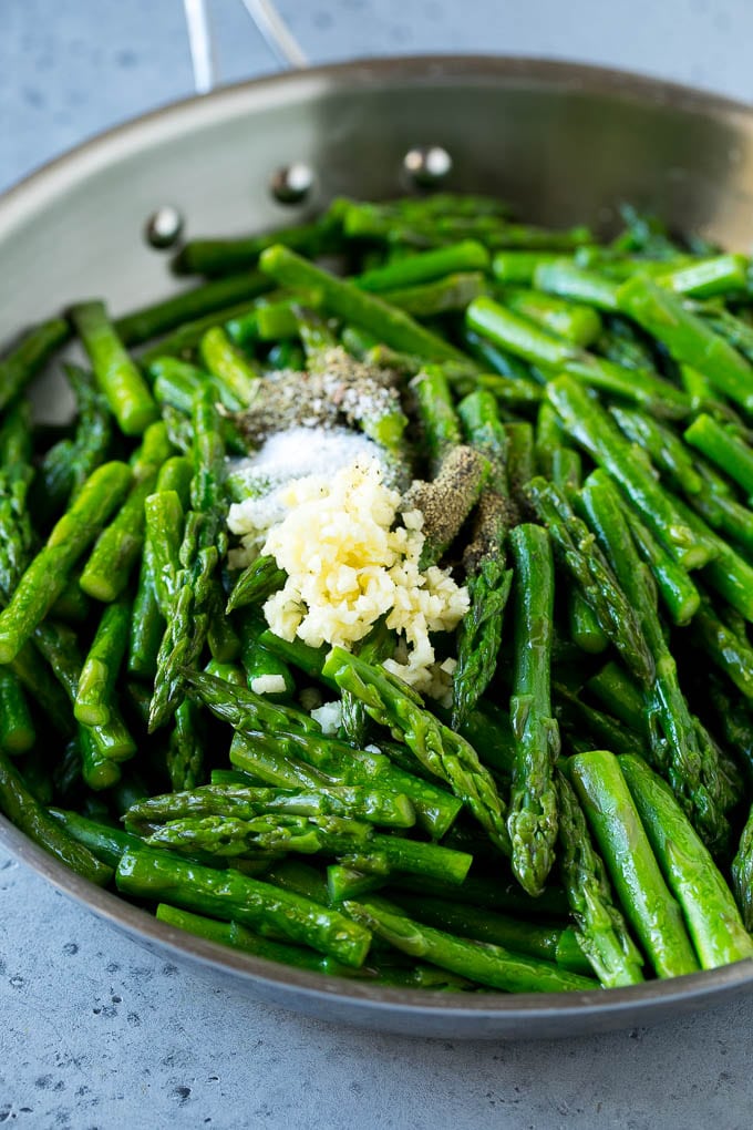 Cooked asparagus stalks in a pan with garlic, herbs and seasonings.