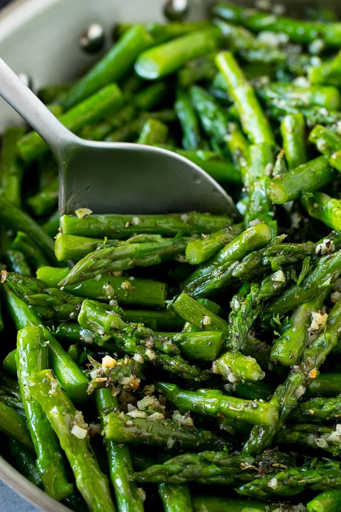 A serving spoon in a pan of garlic and herb sauteed asparagus.