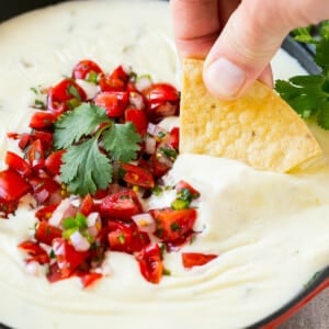 A tortilla chip in a pan of white queso dip.