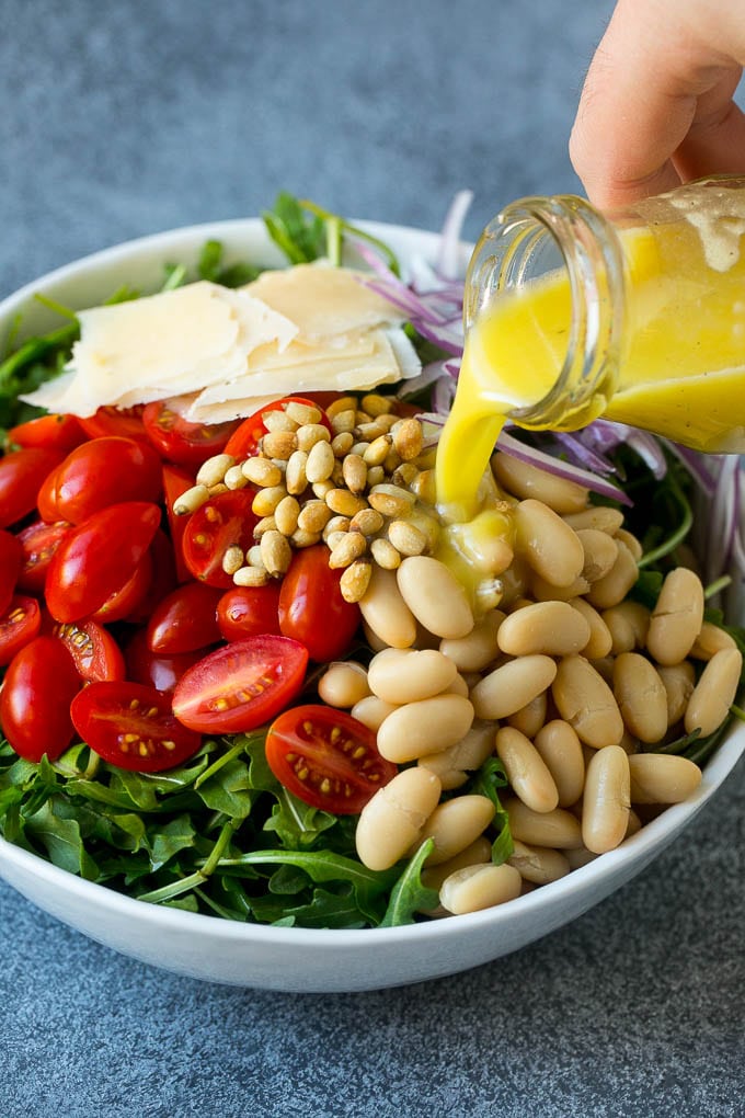 White beans, tomatoes, pine nuts, parmesan and red onion with salad dressing being poured over the top.