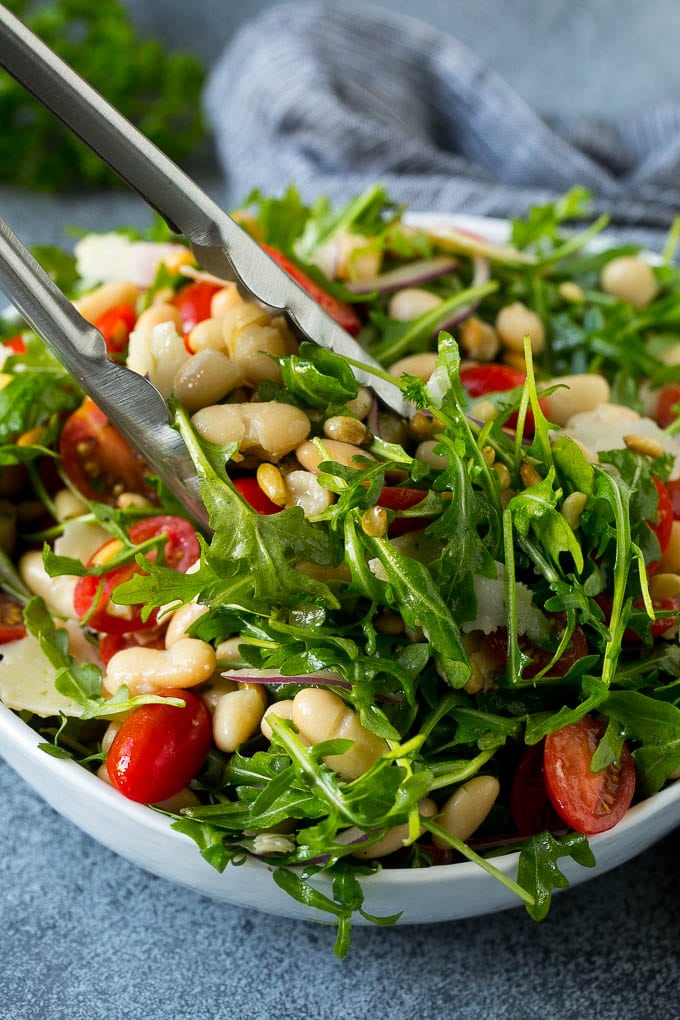 Tongs serving up a portion of arugula salad.