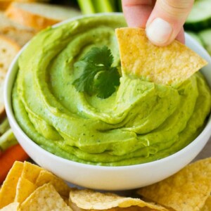 A hand scooping out a portion of avocado dip with a tortilla chip.