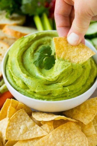 A hand scooping out a portion of avocado dip with a tortilla chip.