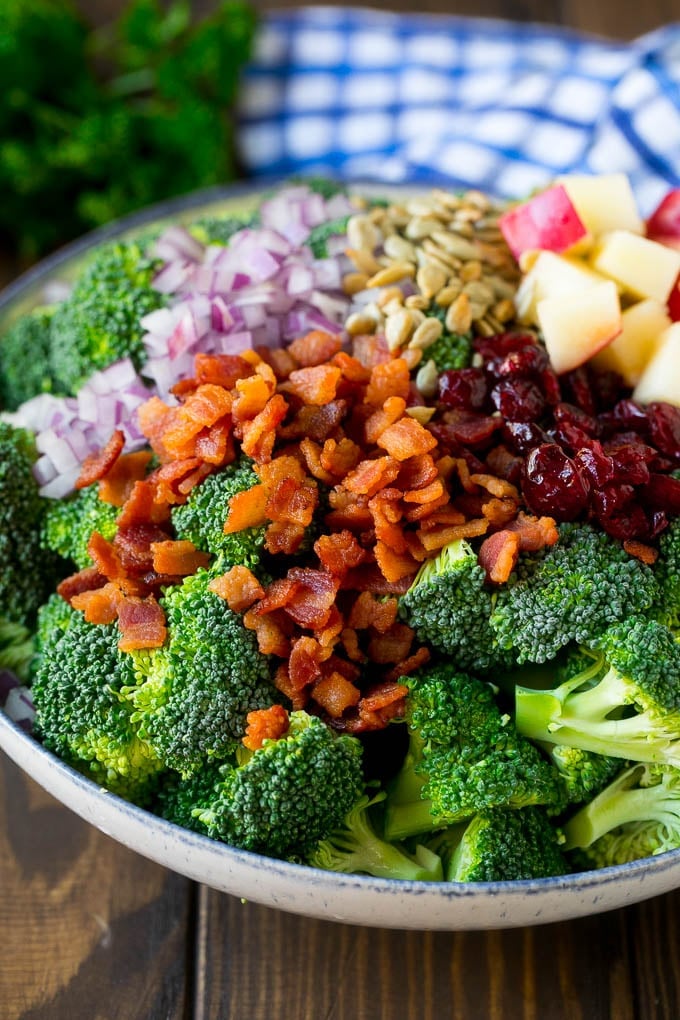 Broccoli florets, bacon, apples, dried cranberries, red onion and sunflower seeds in a bowl.